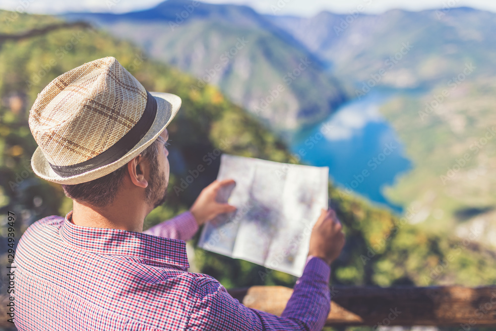 Fototapeta premium Traveler holding map and looking at trekking plan on hill above beautiful canyon landscape.