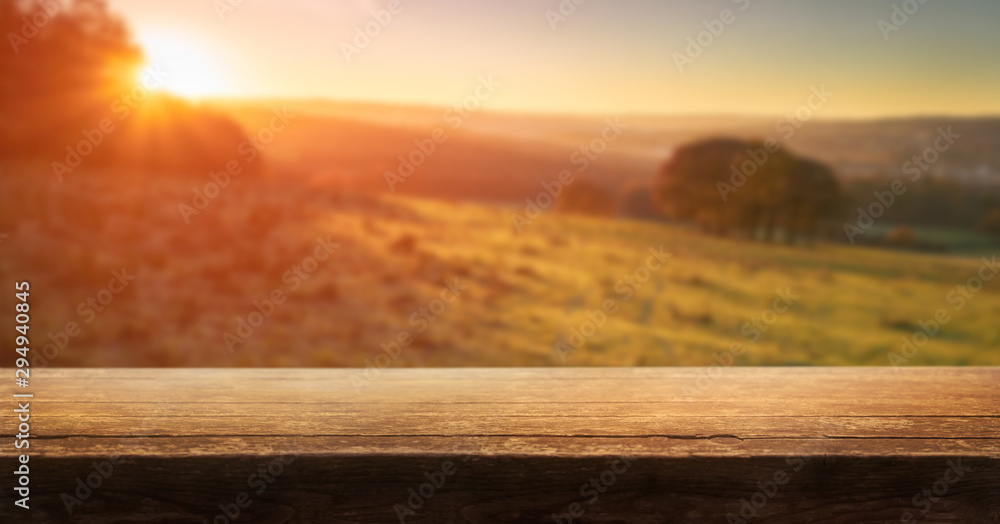 A wooden table top product display with a blurred background scene of golden sunset fields.