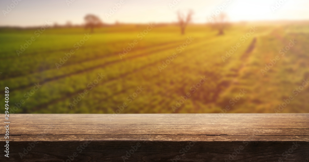 A wooden table top product display with a blurred background scene of farmland at sunset.