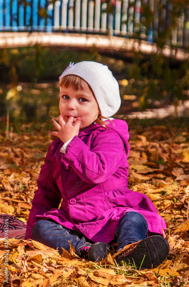 Pretty child suck a ginger in the autumn park in the middle of the orange fallen leaves Pretty child suck a ginger in the autumn park in the middle of the orange fallen leaves