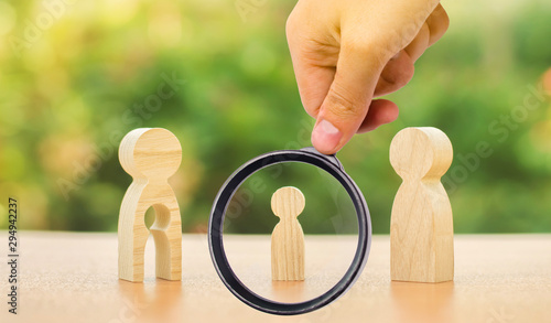 A magnifying glass looks at a child’s figure stands between father and mother. The child chooses which parent to live with after their divorce. Guardianship over child. interest of child photo