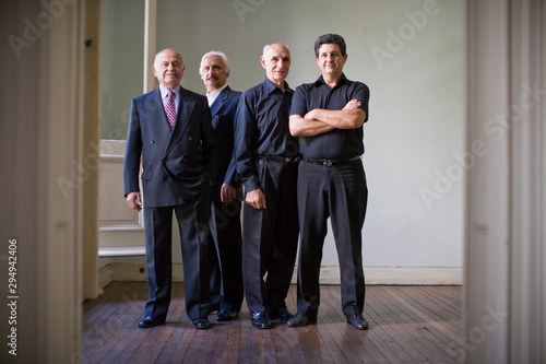 Portrait of a smiling mature adult man folding his arms while standing with three senior adult men in a room. photo