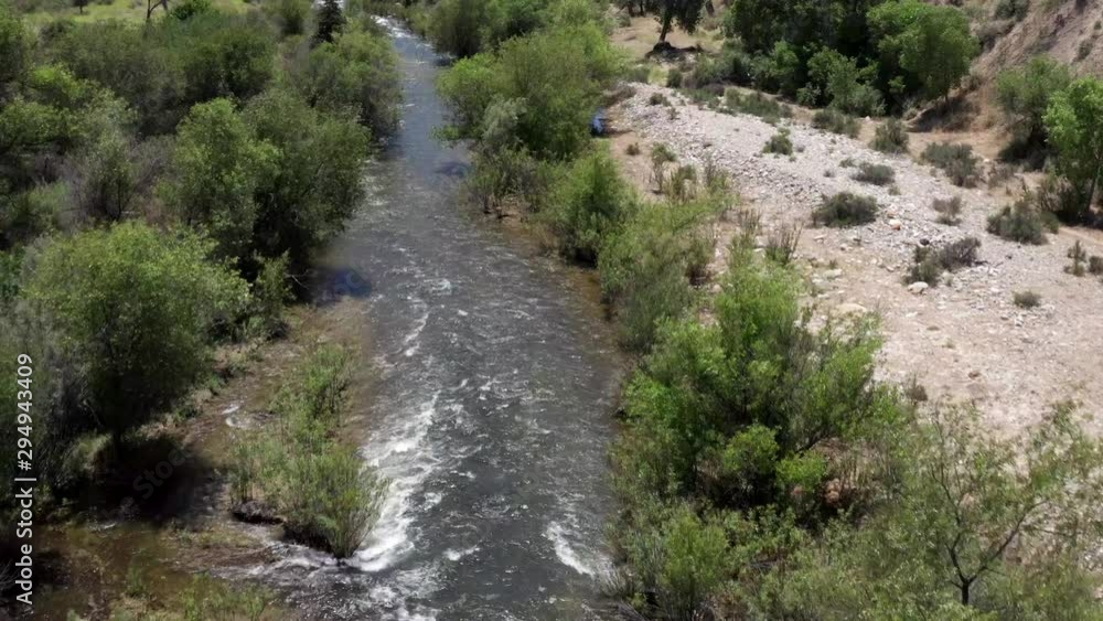 Aerial view above flowing clean river wilderness between woodland trees. Slow forward moving following creek. Aerial view above flowing clean river wilderness between woodland trees. Slow forward moving following creek.