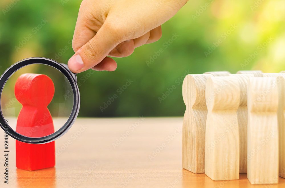 Φωτογραφία A magnifying glass looks at a red figurine of a man stands aside from the crowd of people