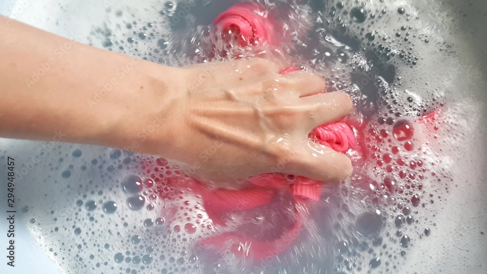 Female hand with blue nails wash a pink T-shirt in a basin