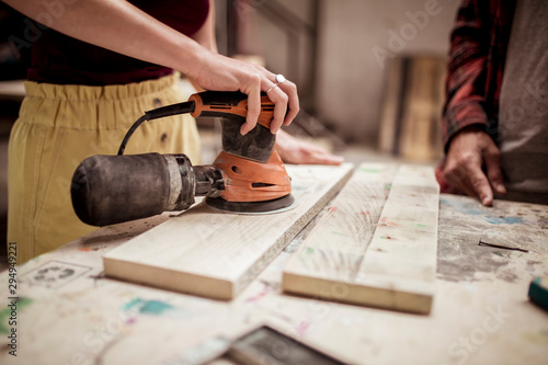 Obraz na plátne Midsection of female carpenter sanding wood while standing by male colleague at
