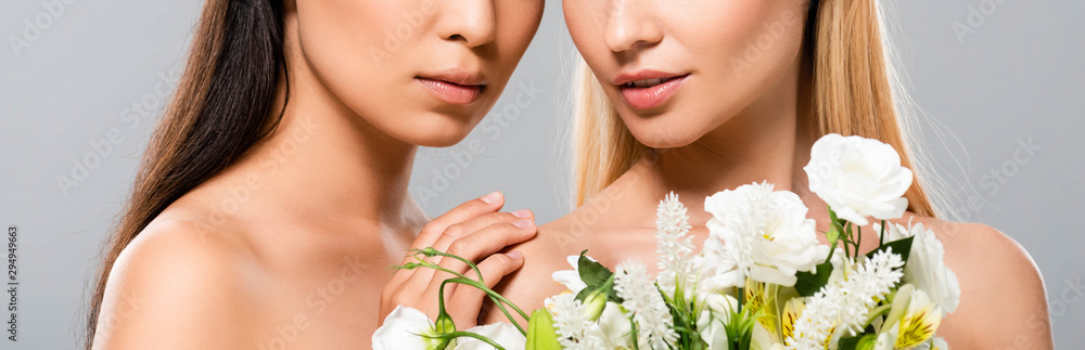 cropped view of blonde and brunette naked women with flowers isolated on grey, panoramic shot