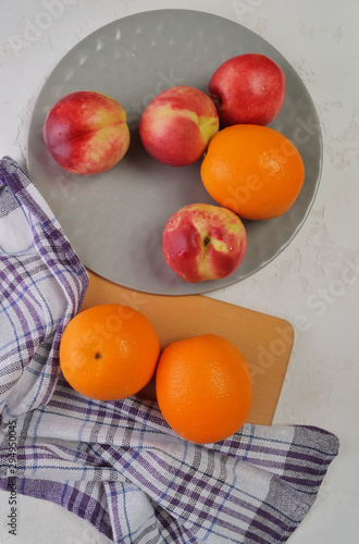 Juicy oranges and red nectarines on a light table.Fresh fruits in a gray plate, top view.