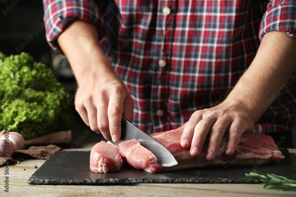 Man cutting fresh raw meat on wooden table, closeup Man cutting fresh raw meat on wooden table, closeup