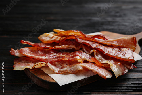 Slices of tasty fried bacon on black wooden table, closeup photo