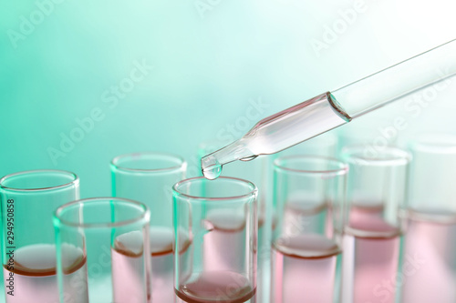 Dropping sample into test tube with liquid on color background, closeup