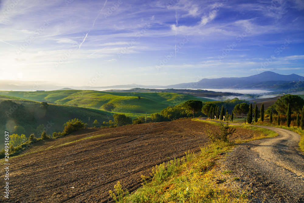 Beautiful view of green fields and meadows at sunrise in Tuscany