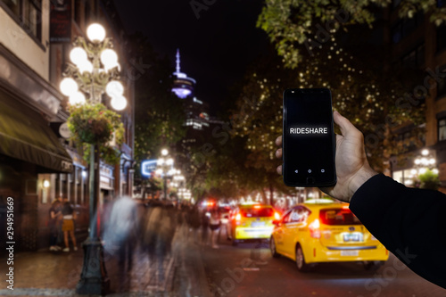 A cell phone with the the words rideshare on the screen superimposed over a view of a city street in Downtown Vancouver. photo