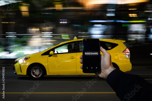 A cell phone with the the words rideshare on the screen on in front of a yellow taxi in the background. photo
