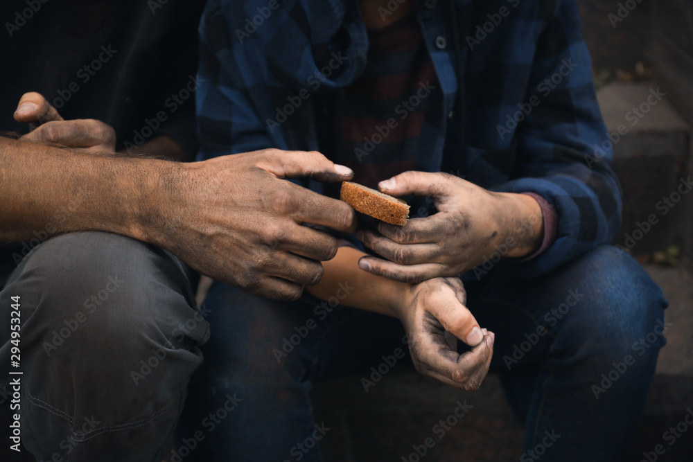 Poor homeless people sharing piece of bread outdoors, closeup