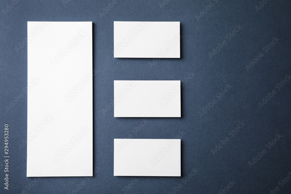 Blank business cards and paper sheet on dark grey background, flat lay. Mock up for design Blank business cards and paper sheet on dark grey background, flat lay. Mock up for design
