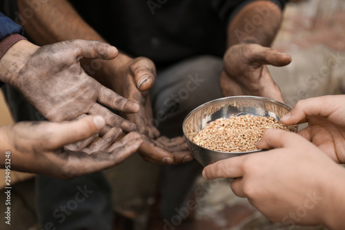 Woman giving poor homeless people bowl of wheat outdoors, closeup photo