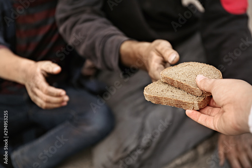 Tableau sur toile Woman giving poor homeless people pieces of bread outdoors, closeup