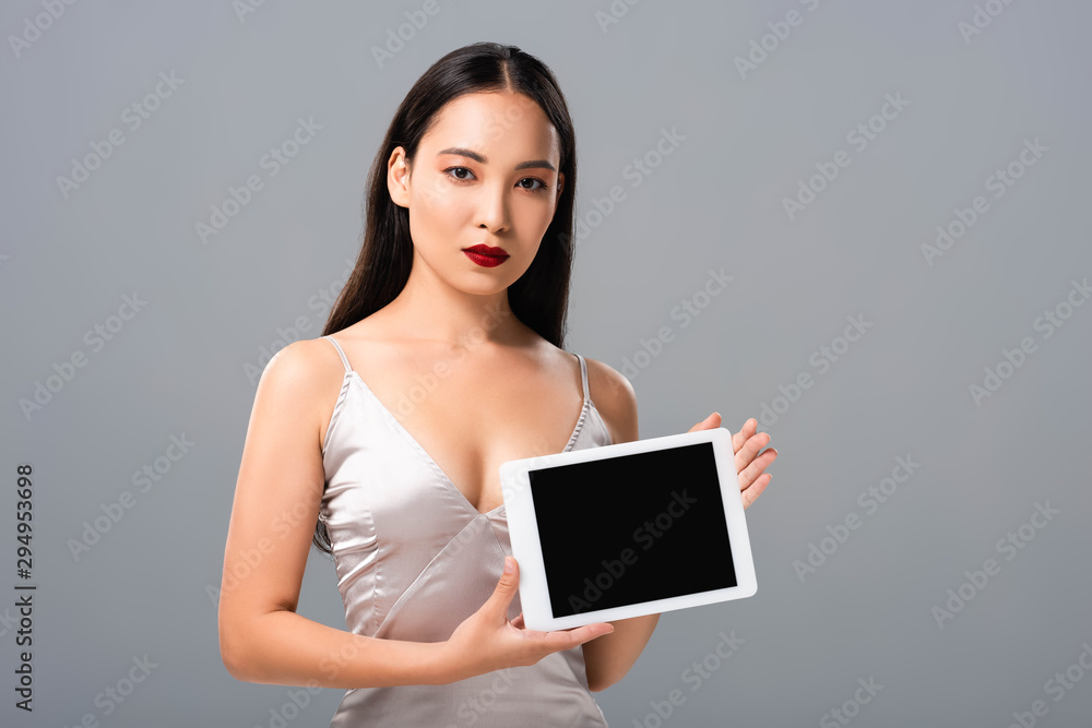 beautiful asian woman in satin dress with red lips holding digital tablet with blank screen isolated on grey beautiful asian woman in satin dress with red lips holding digital tablet with blank screen isolated on grey