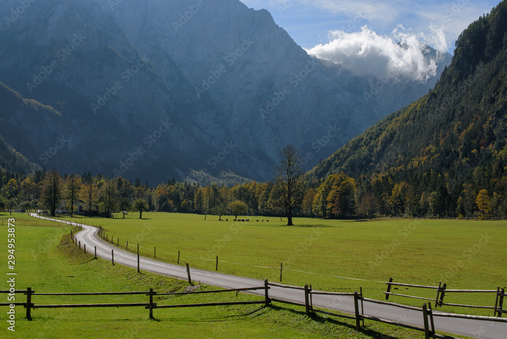Early autumn in Logarska dolina (Logar valley) in Slovenia; beautiful landscape with green grass, road and wooden fence in the foreground, and with the mountain peaks and clouds in the background