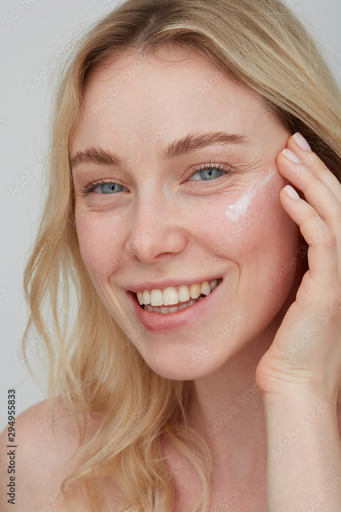 Portrait of smiling young woman applying cream on her face Portrait of smiling young woman applying cream on her face