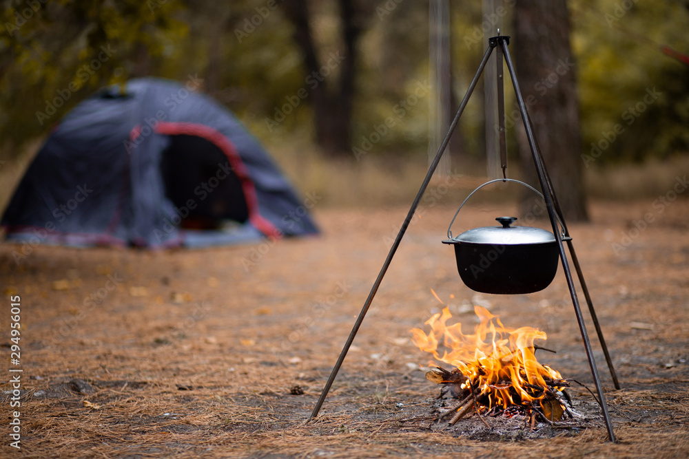 Hiking pot in bonfire with blue tent in autumn forest traveling Hiking pot in bonfire with blue tent in autumn forest traveling