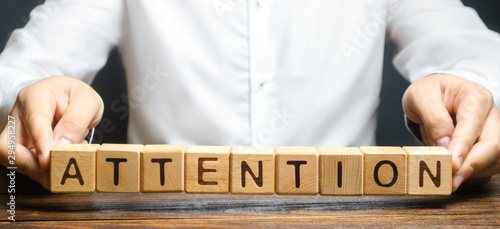 A man holds the word Attention in his hands. Focus on the point. Self-discipline and perseverance. In the spotlight. teacher, superior. Pay attention to important topics