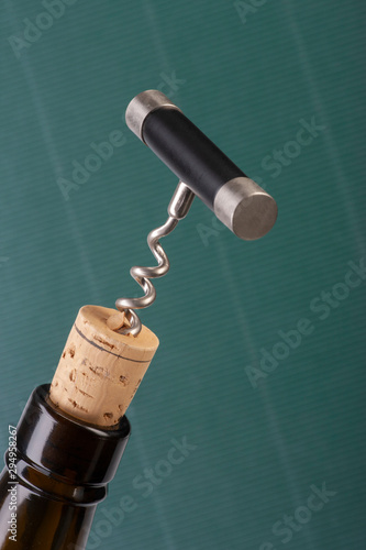 Corkscrew and wine bottle over green background