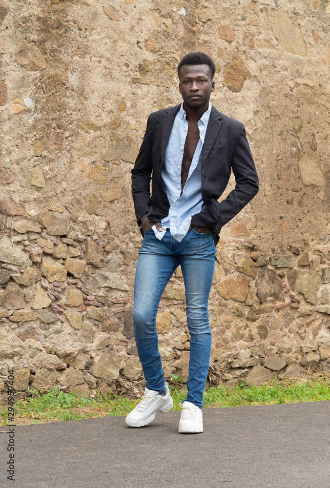 Hombre joven negro de Senegal con chaqueta, camisa y pantalones estrechos,  sobre un fondo de piedra. Stock-foto | Adobe Stock