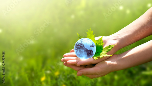 Fototapeta Naklejka Na Ścianę i Meble -  Earth crystal glass globe ball and maple leaf in human hand on grass background. Saving environment, save clean green planet, ecology concept. Card for World Earth Day.