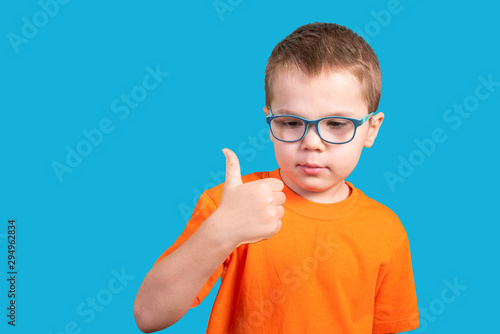 Little boy in glasses shows thumb up. Isolated on a blue background.