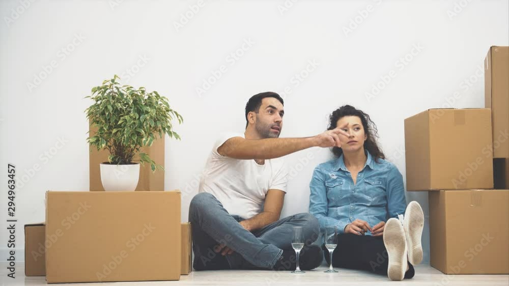 Happy couple is talking while sitting on the floor and holding glasses of white wine. Action. 4K. Happy couple is talking while sitting on the floor and holding glasses of white wine. Action. 4K.