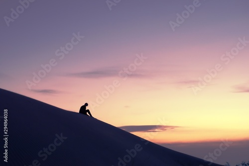 Lone woman contemplating the horizon in the desert from atop a dune against a golden sky at sunset.