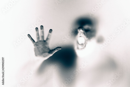 Creepy looking man is screaming behind a frosted glass. photo