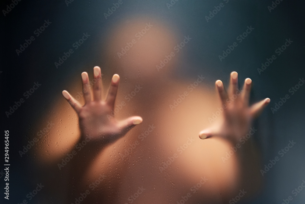 Creepy man looking behind the frosted glass and holding it with two hands.