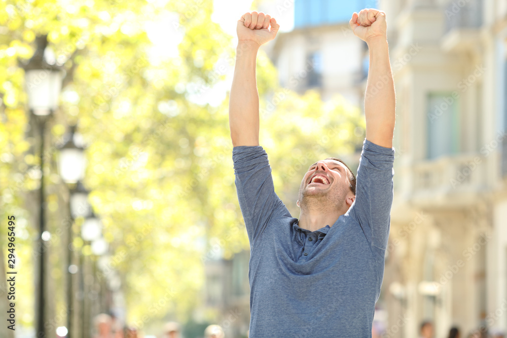 Excited man raising arms celebrating success in the street