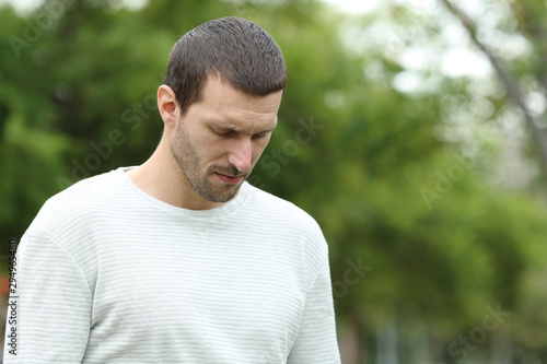 Sad man walking alone looking down in a park