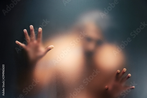 Fototapeta Naklejka Na Ścianę i Meble -  Creepy man looking behind the frosted glass and holding it with two hands.