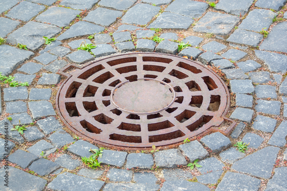 Manhole cover near paving stones. Rusty manhole cover on the walkside with paving stones Manhole cover near paving stones. Rusty manhole cover on the walkside with paving stones