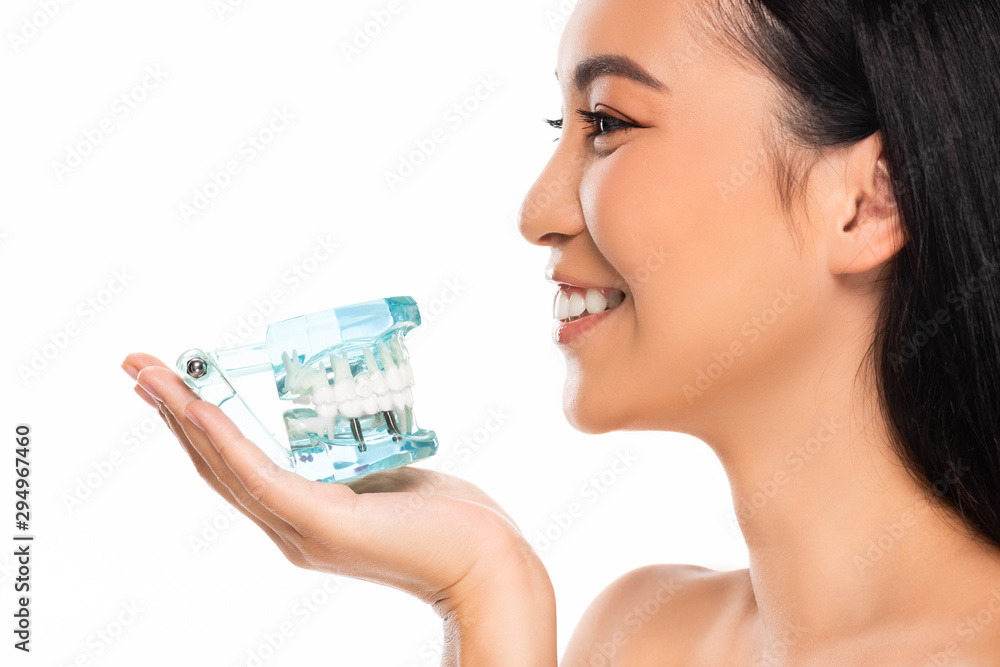 side view of smiling naked asian woman holding jaw model isolated on white side view of smiling naked asian woman holding jaw model isolated on white