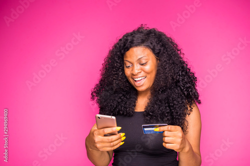 a beautiful young african nigerian lady feels happy what she is doing with her smart phone and credit card