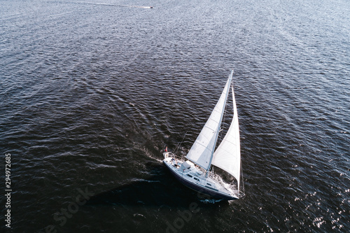 Aerial photography of yacht with white sails in dark blue open space. The good wind fills sails on a sunny summer day. © valdisskudre