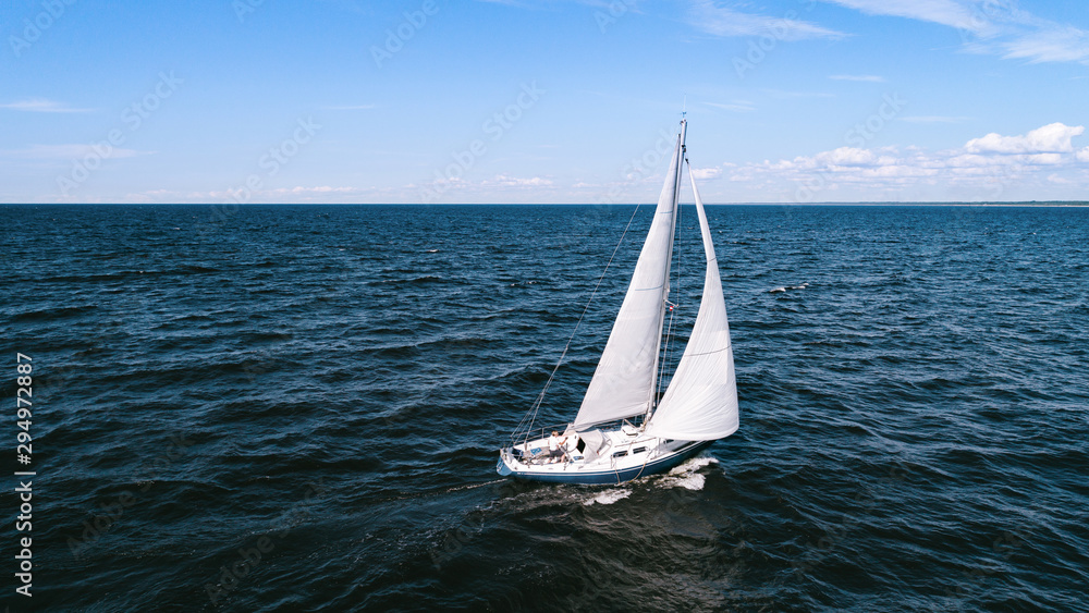 Fototapeta premium Aerial photography of yacht with white sails in dark blue open space. The good wind fills sails on a sunny summer day.
