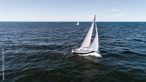 Aerial photography of yacht with white sails in dark blue open space. The good wind fills sails on a sunny summer day. © valdisskudre