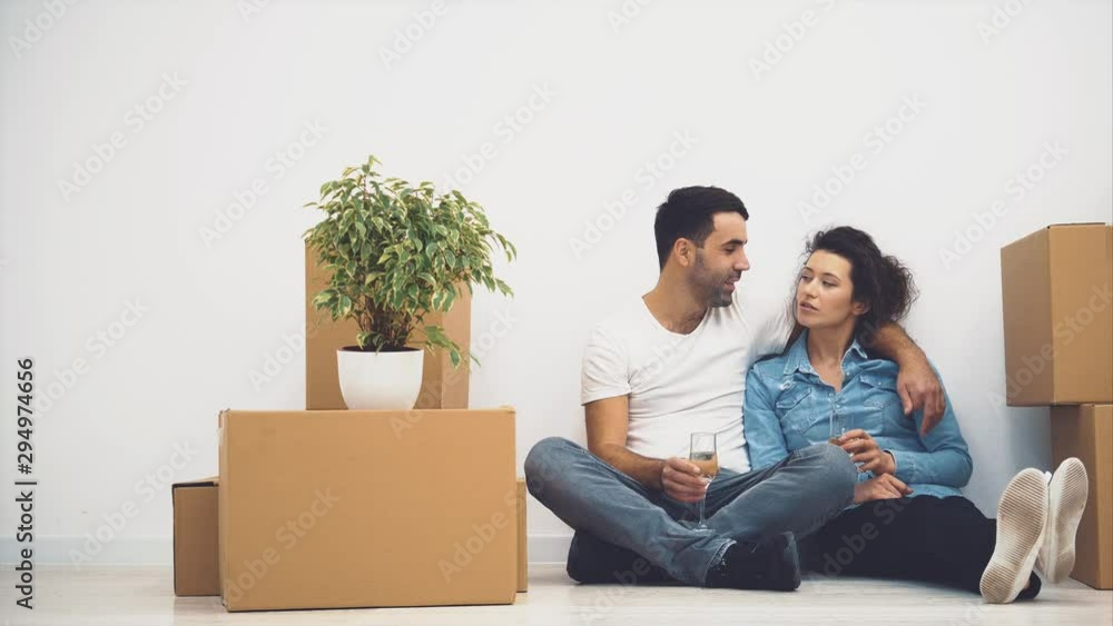 Happy couple is talking while sitting on the floor and holding glasses of white wine. Action. 4K. Happy couple is talking while sitting on the floor and holding glasses of white wine. Action. 4K.