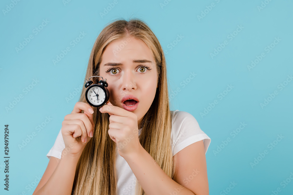 Fototapeta premium beautiful young blonde woman with alarm clock showing time isolated over blue