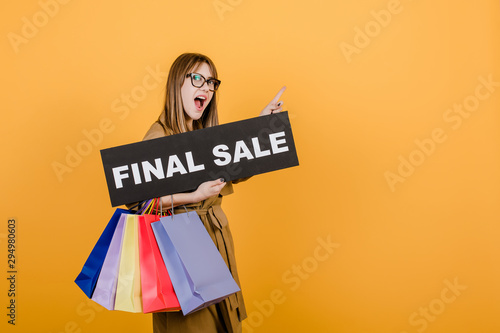 hipster woman in glasses and coat with final sale sign and colorful shopping bags isolated over yellow © Anastasia