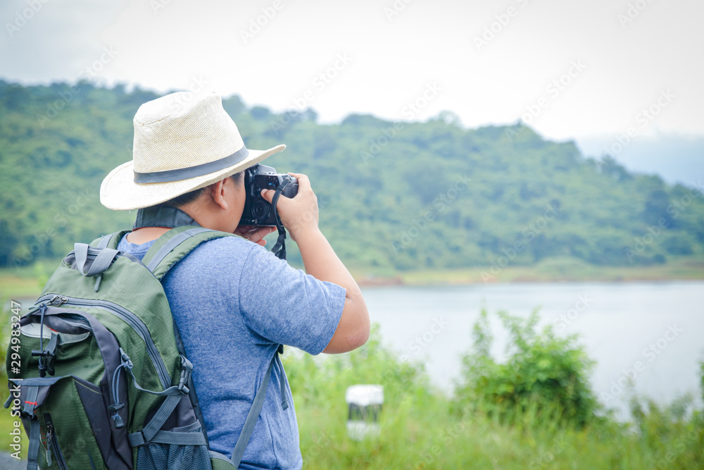 A small Asian boy wearing a hat likes to travel to nature. Hold the camera to take a landscape photo