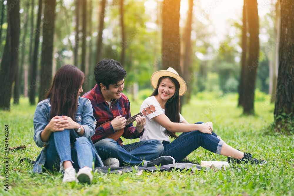A group of young people playing ukulele while sitting together in the park A group of young people playing ukulele while sitting together in the park