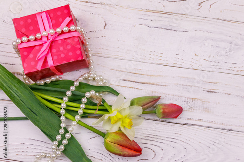 Fototapeta Naklejka Na Ścianę i Meble -  Gift box, pearl necklace and bouquet of red tulips and daffodils on wooden background. Concept of Valentine's Day, Women's Day, Mother's Day and Birthday. Top view, copy space